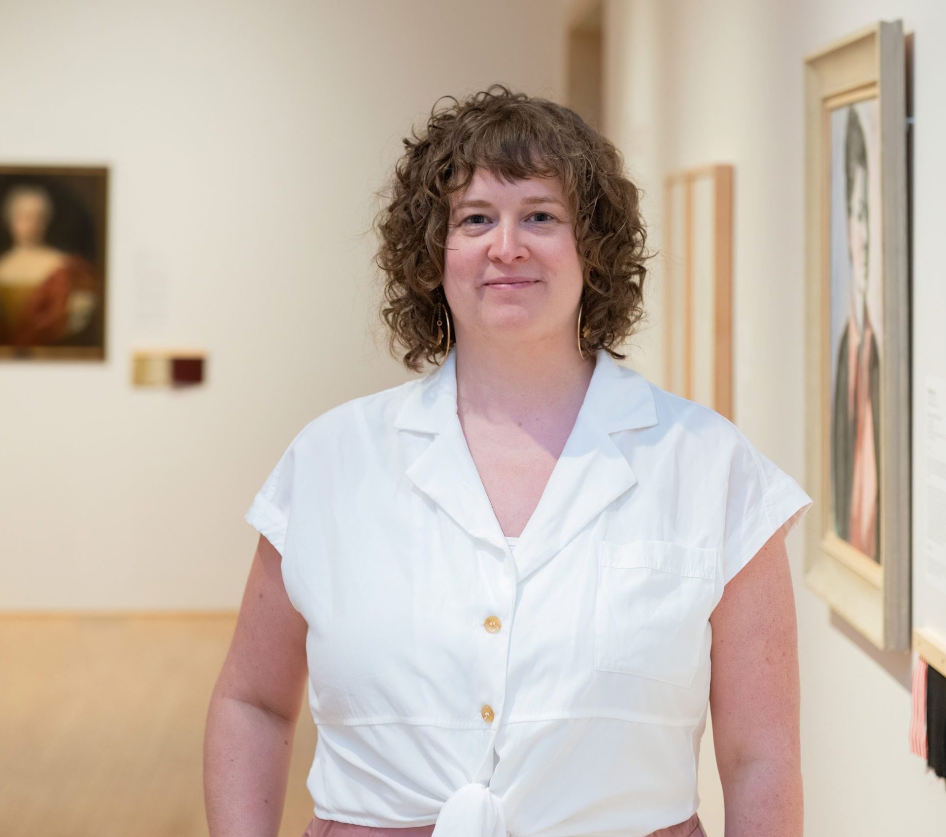 Gallery curator Anik Glaude stands in a gallery space, wearing a white shirt and smiling.