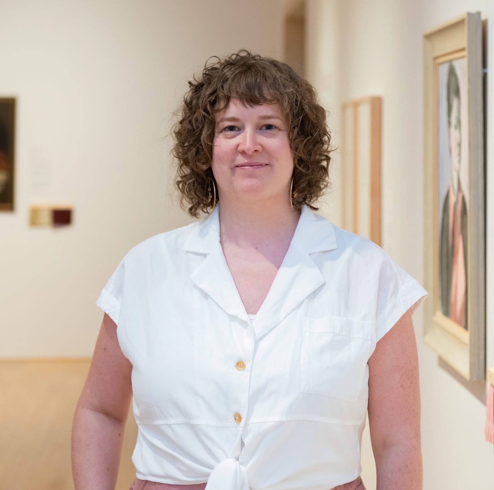 Gallery curator Anik Glaude stands in a gallery space, wearing a white shirt and smiling.