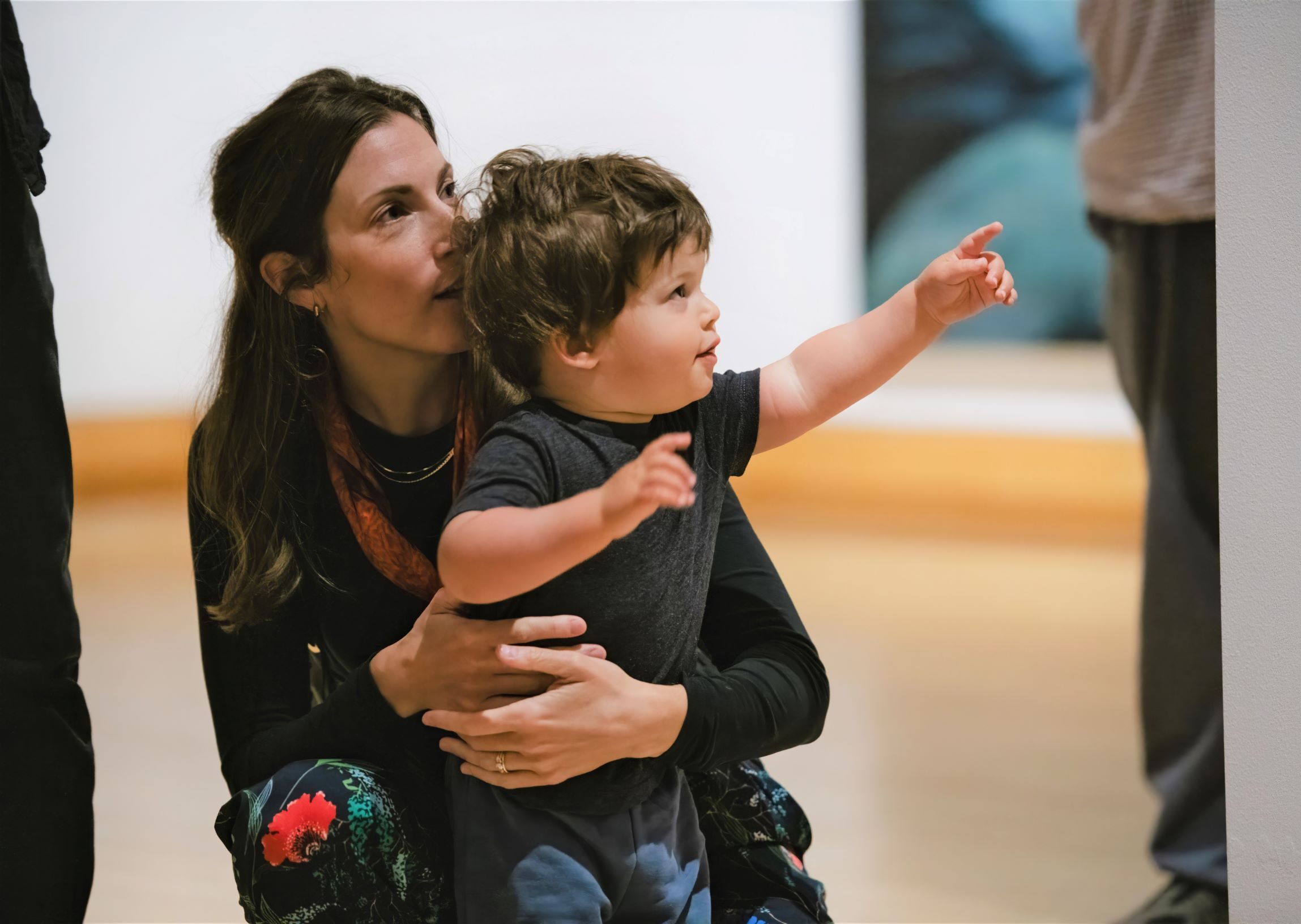 A mother holds her young son as he points to an artwork.