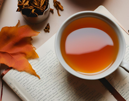 A cup of tea on a journal surrounded by leaves orange leaves and dried tea.