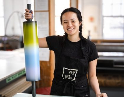 A woman smiling holding an ink roller used in printmaking.