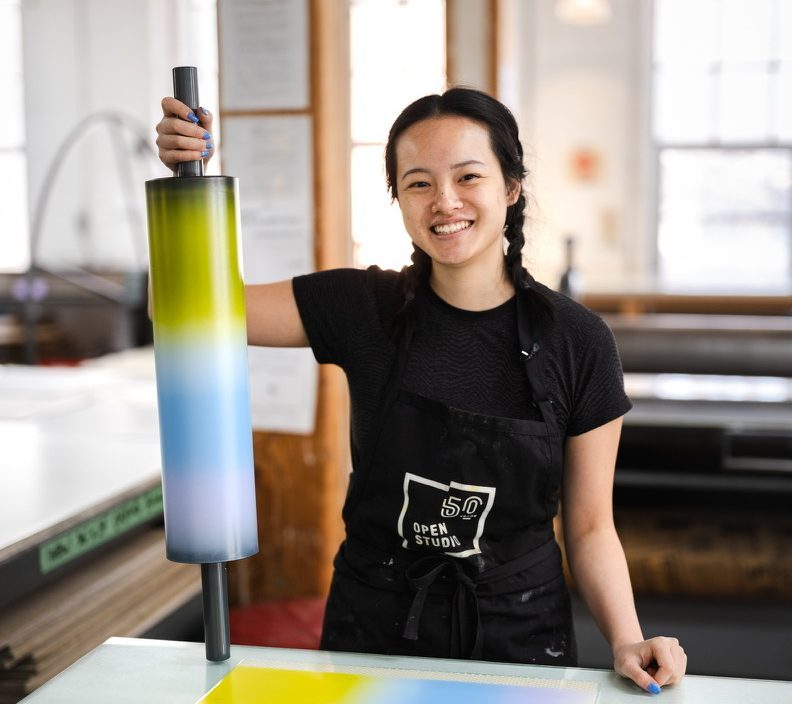 A woman smiling holding an ink roller used in printmaking.