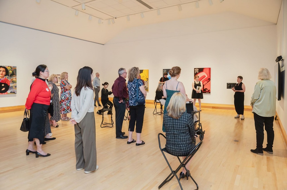 A group of people listening to an artist talk in front of her work in the gallery.