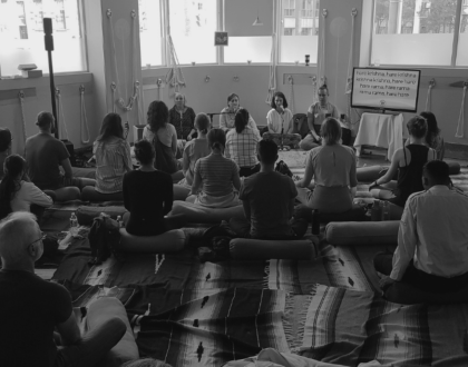 A group of people sitting on the ground, practicing kirtan.