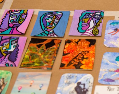 Eight colourful artist trading cards displayed on a brown surface.