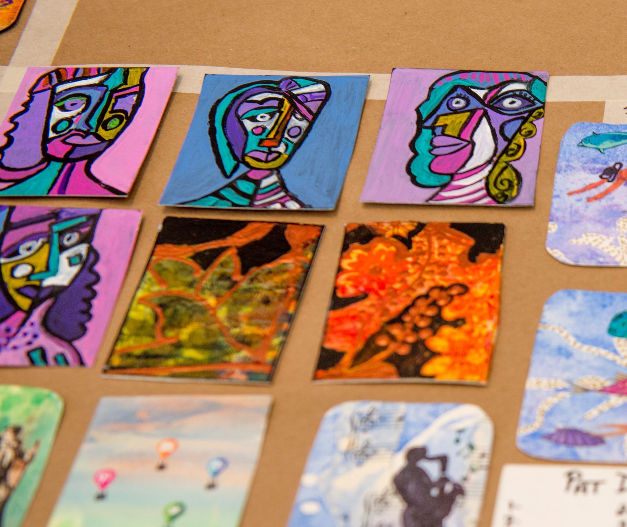 Eight colourful artist trading cards displayed on a brown surface.