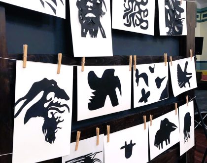 12 papercut artworks handing on a black wall.
