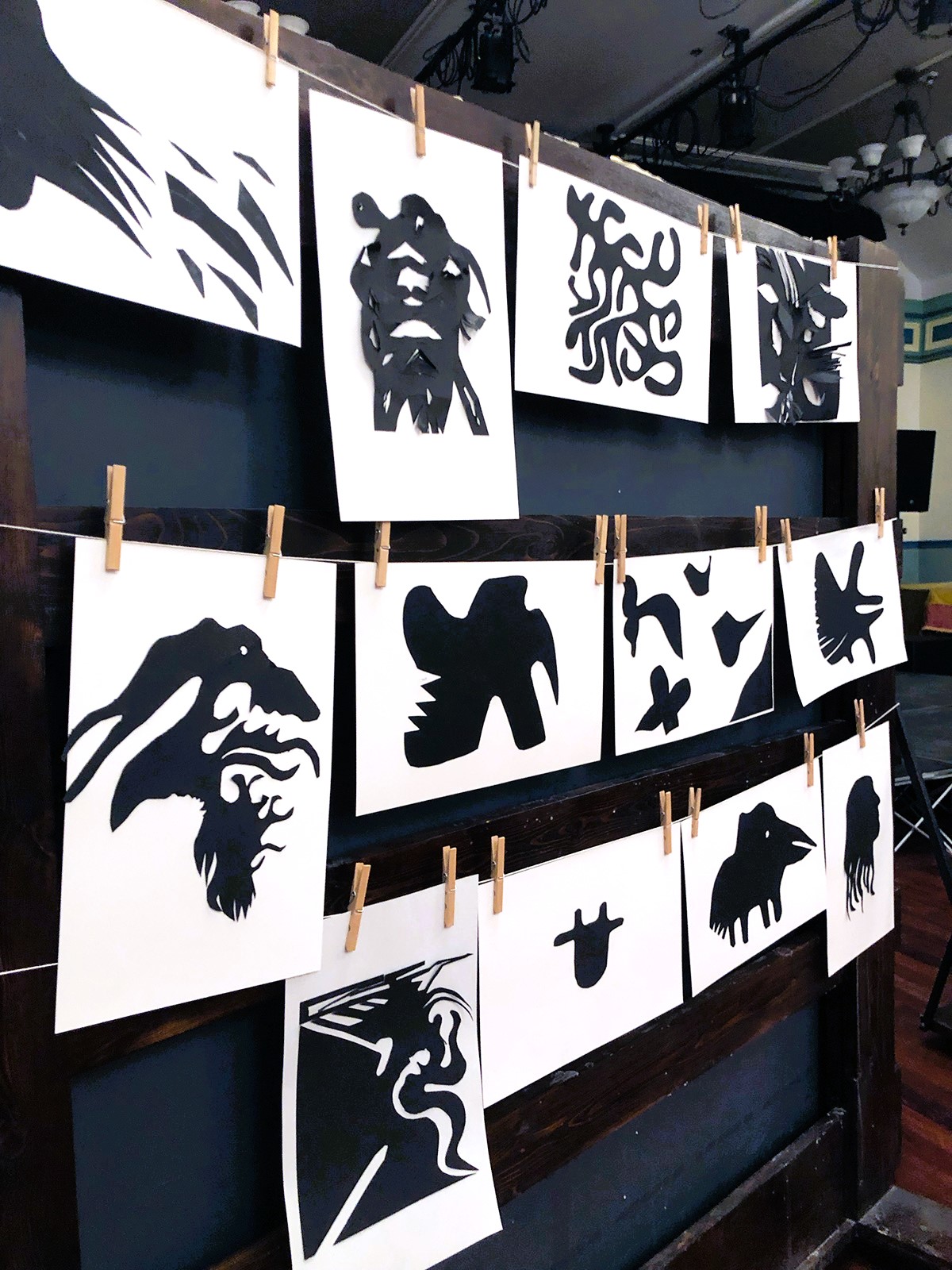 12 papercut artworks handing on a black wall.